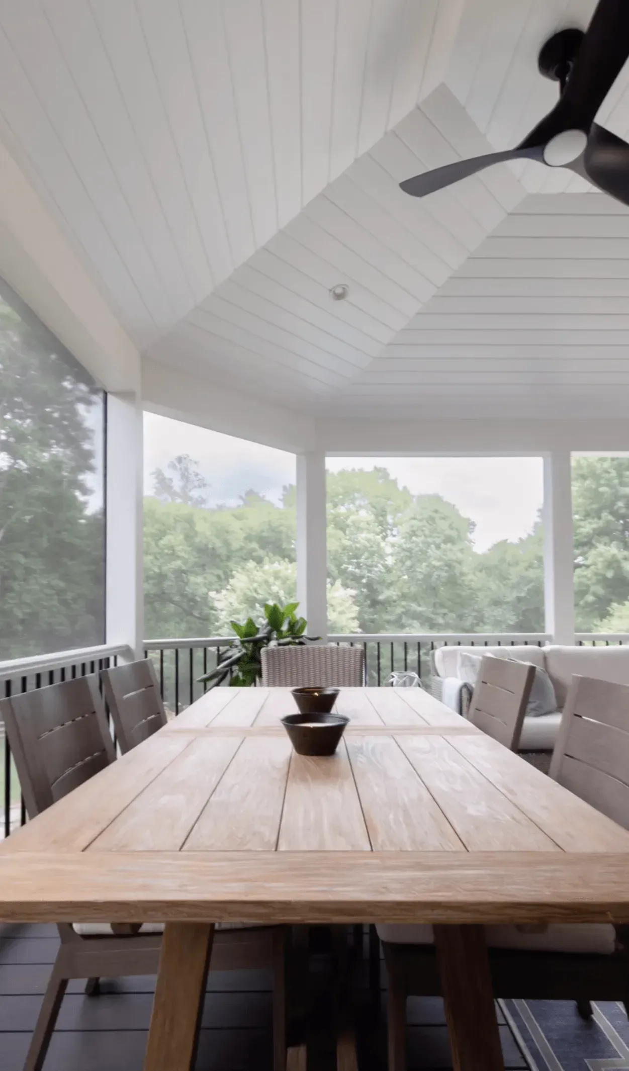 A screened in porch with a table and chairs and a ceiling fan.