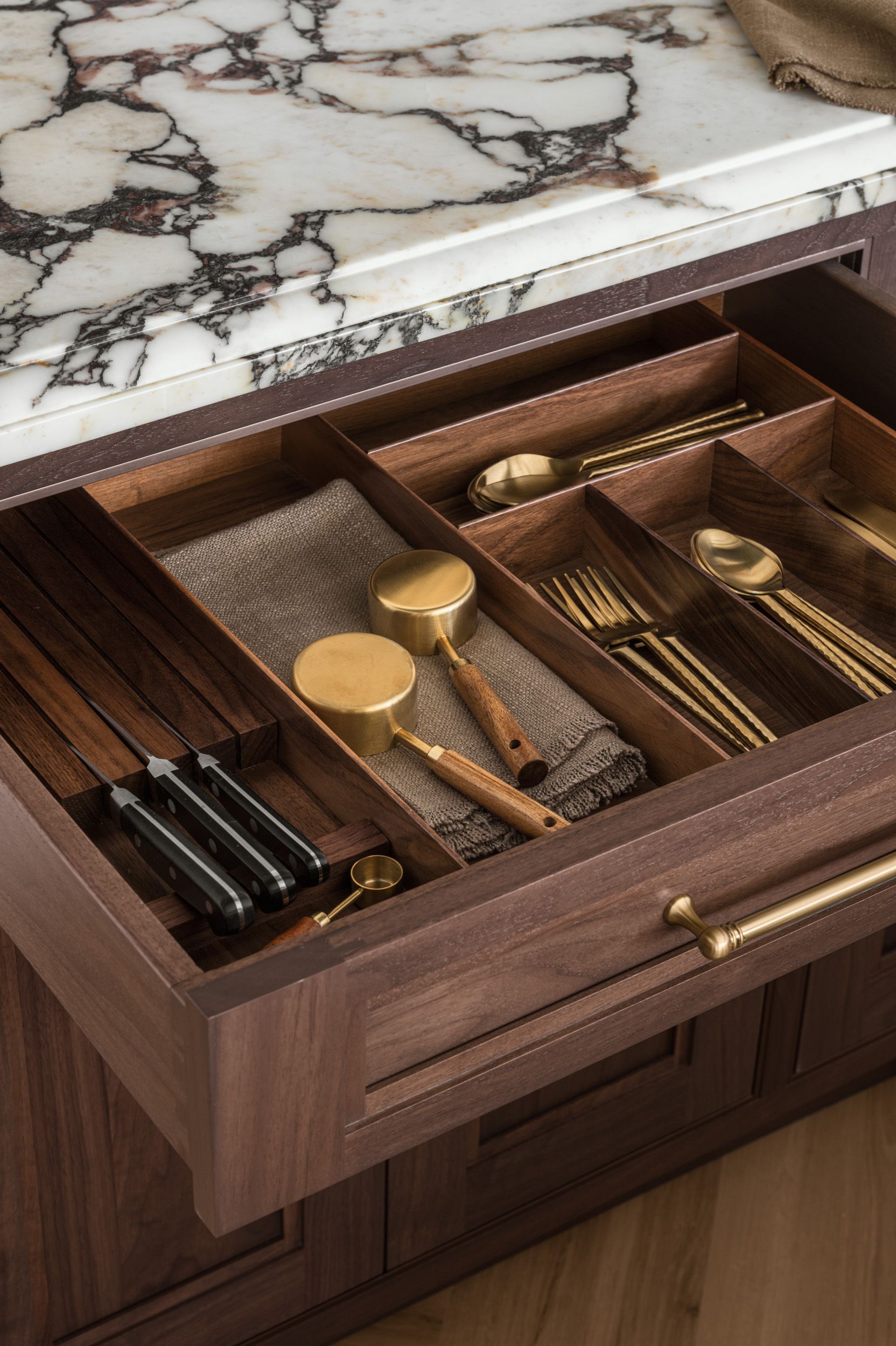 A wooden drawer filled with utensils and a napkin.