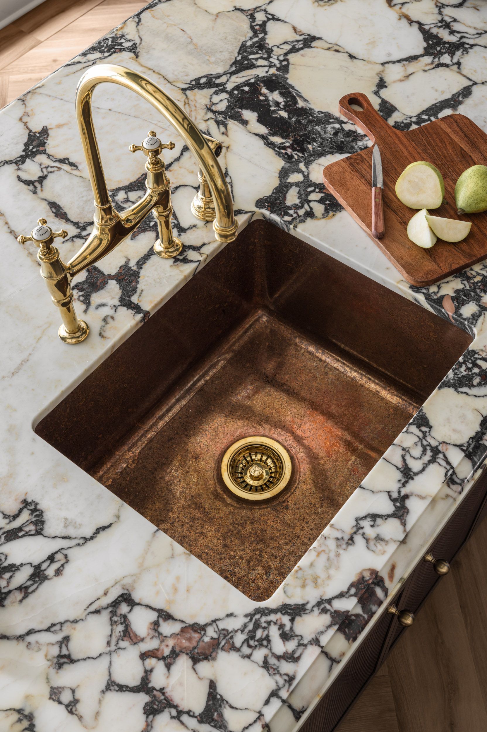 A kitchen sink with a gold faucet on a marble counter top.