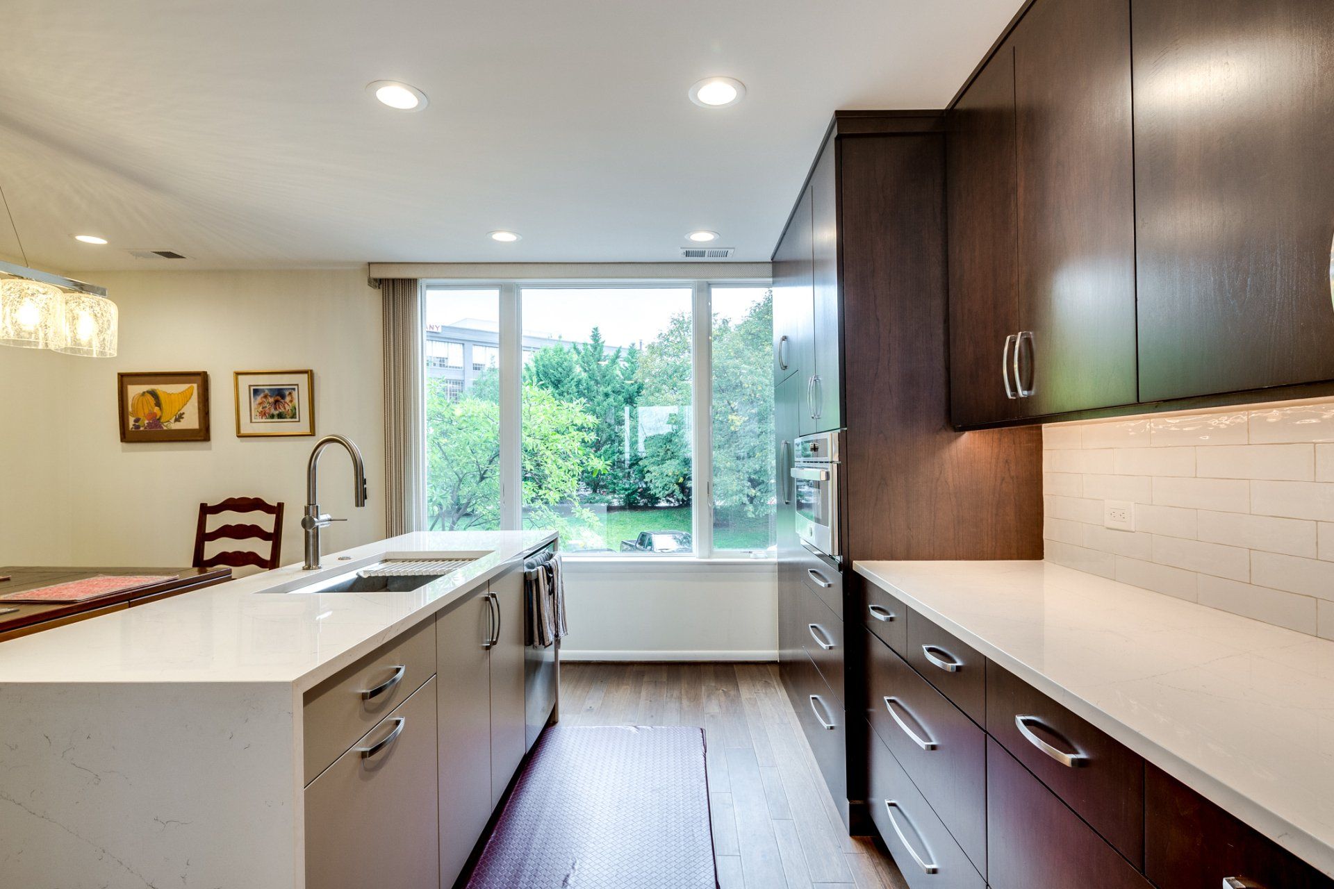 A kitchen with a sink , cabinets , and a large window.
