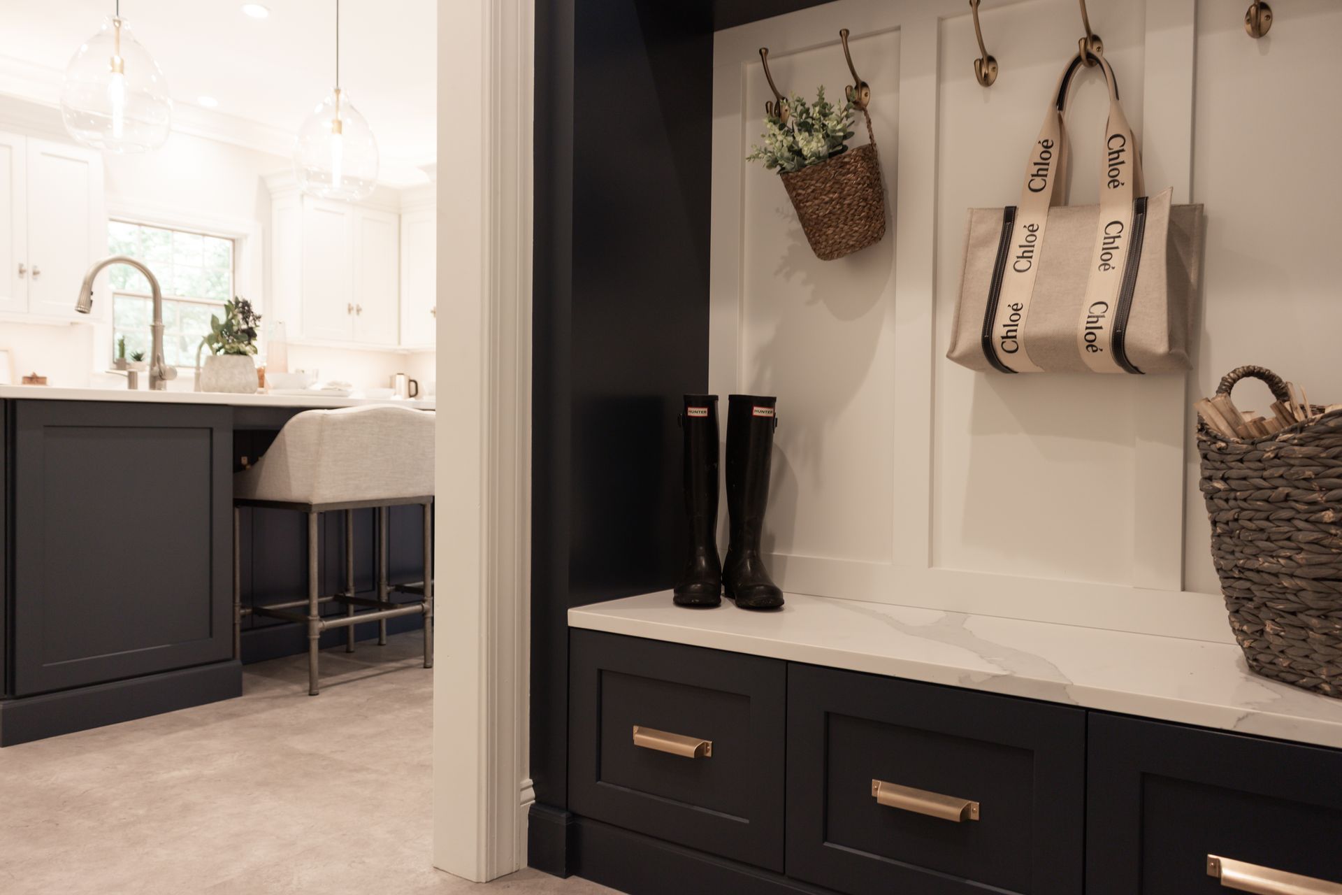 A mud room with a bench , boots , a basket and a bag hanging on the wall.
