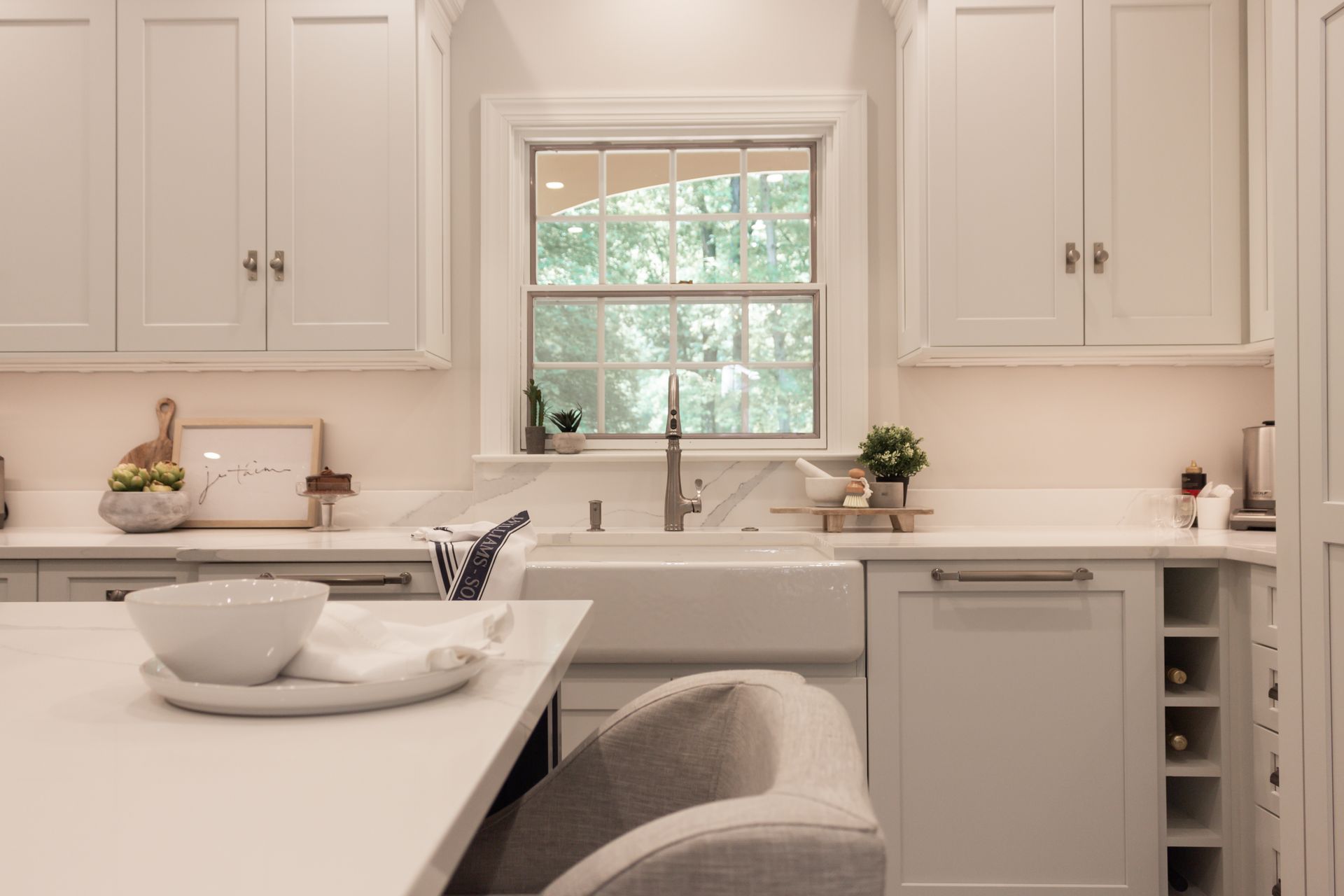 A kitchen with white cabinets , a sink , and a window.
