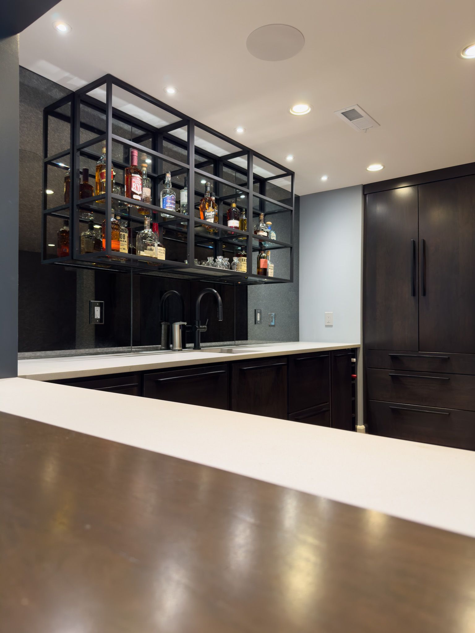 A kitchen with a bar and lots of bottles on shelves