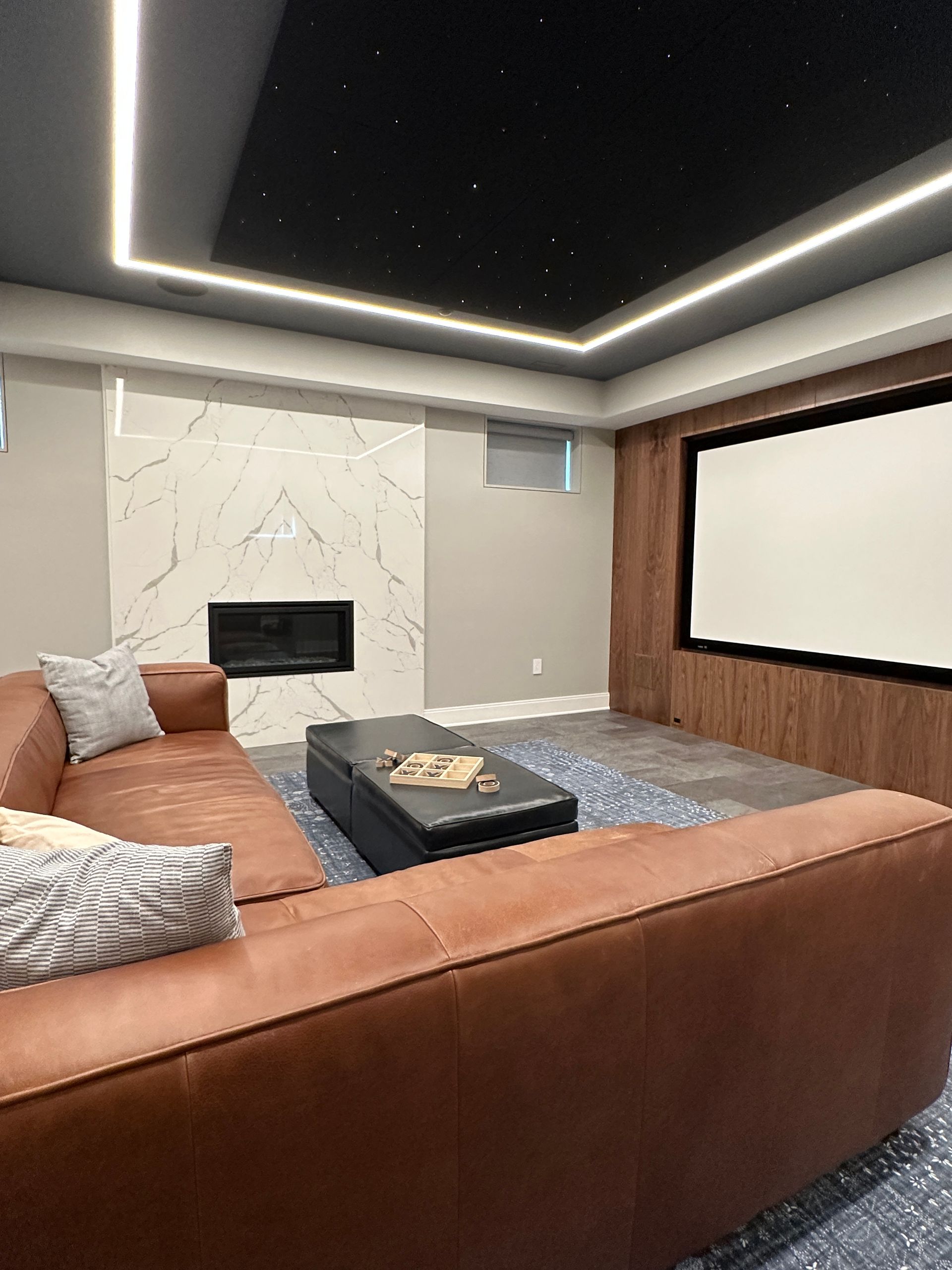 A living room with a couch , ottoman , fireplace and a projector screen.