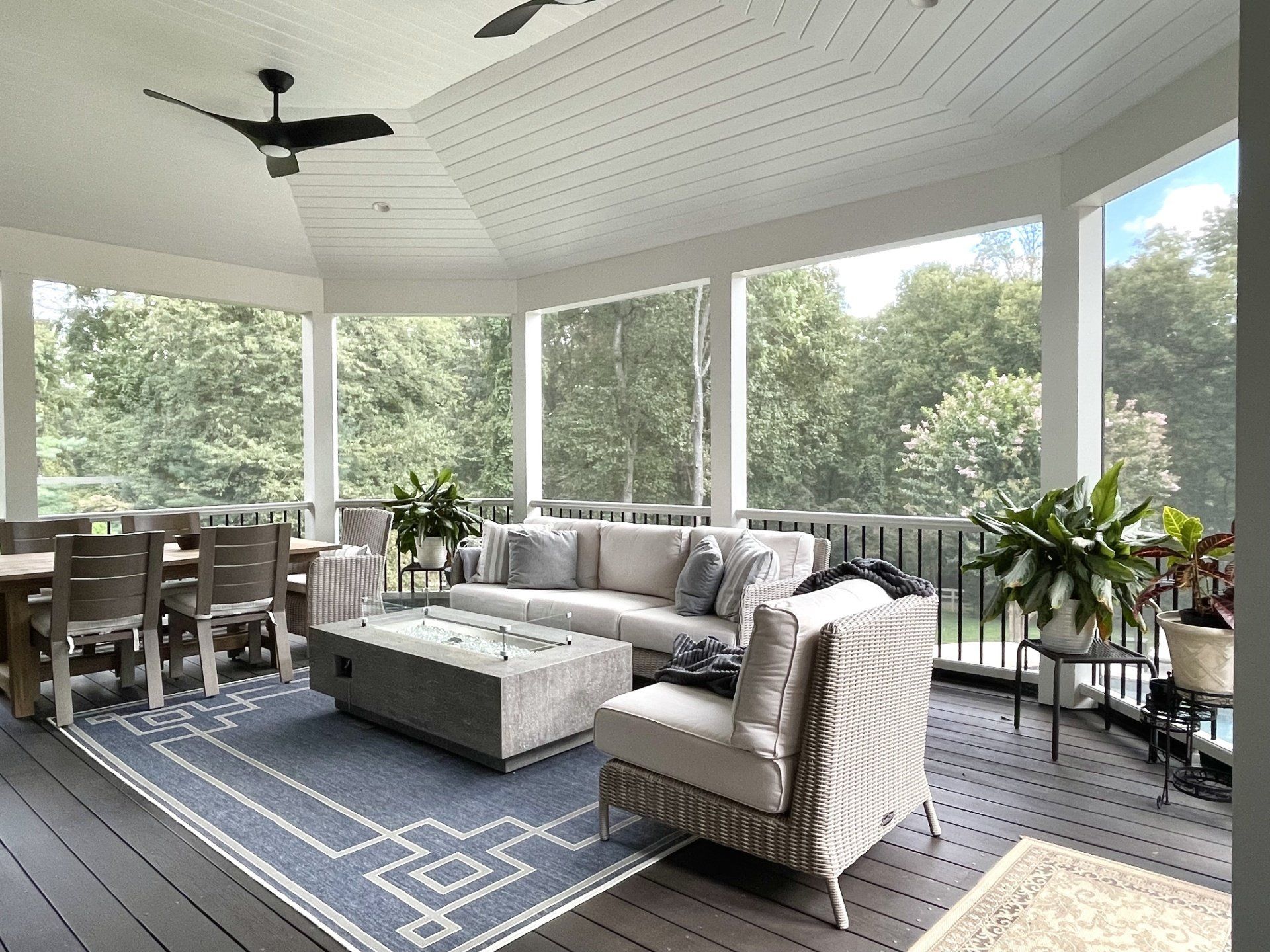 A screened in porch with a couch , chairs , table and ceiling fan.