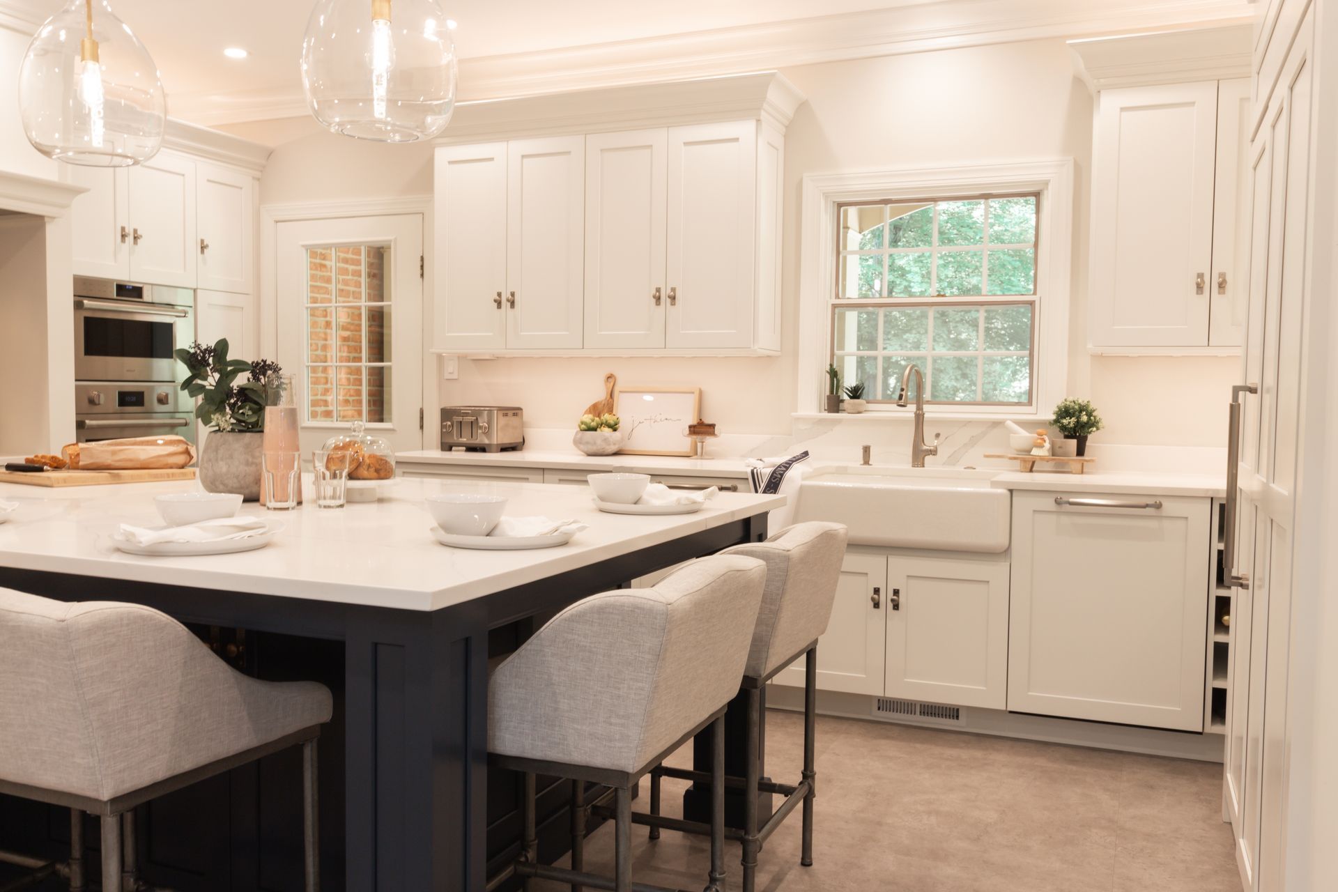 A kitchen with white cabinets , a large island , stools , a sink and a window.