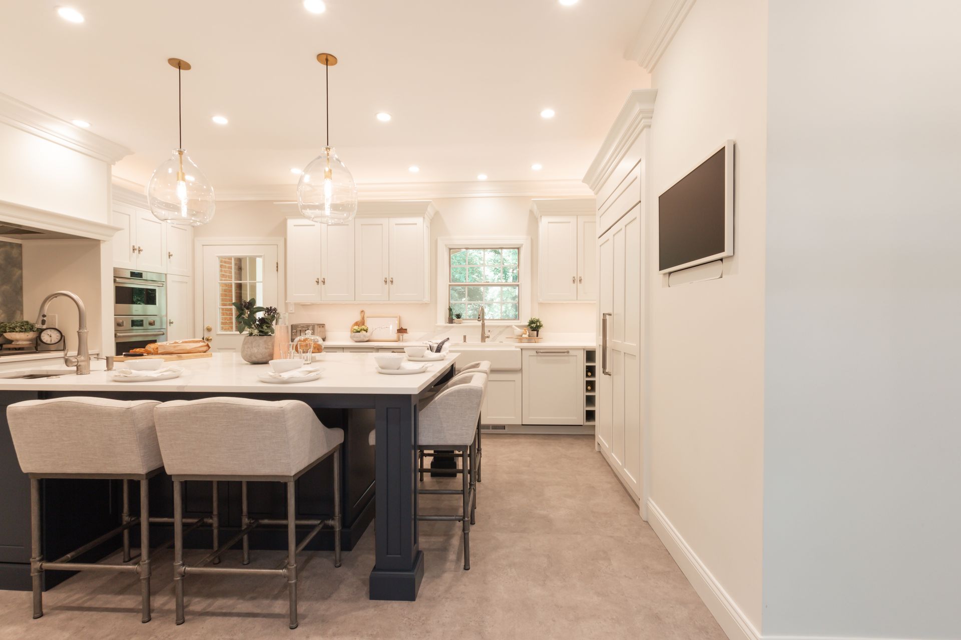 A kitchen with a large island and stools and a flat screen tv on the wall.