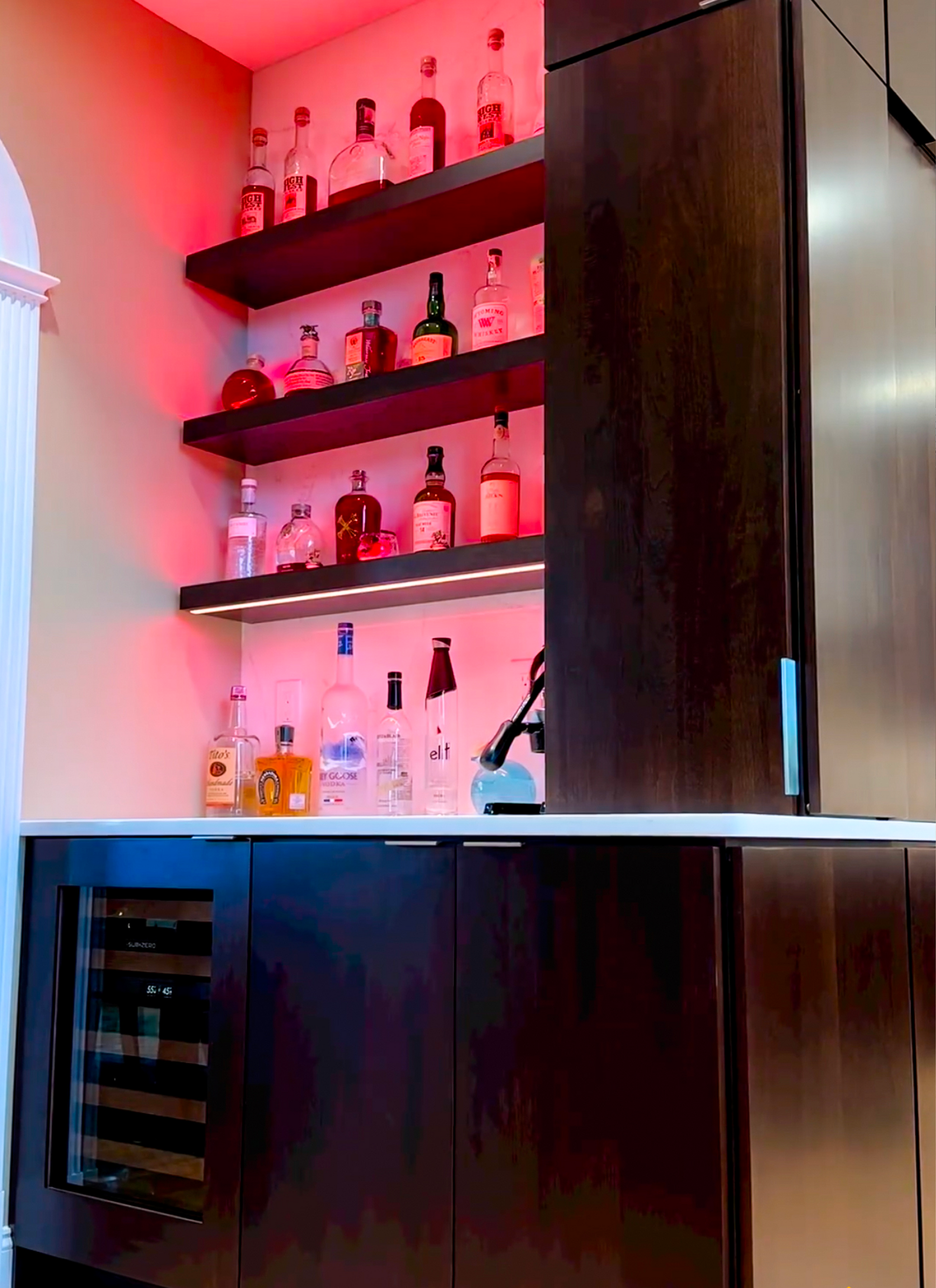 There are many bottles of alcohol on the shelves in the kitchen.