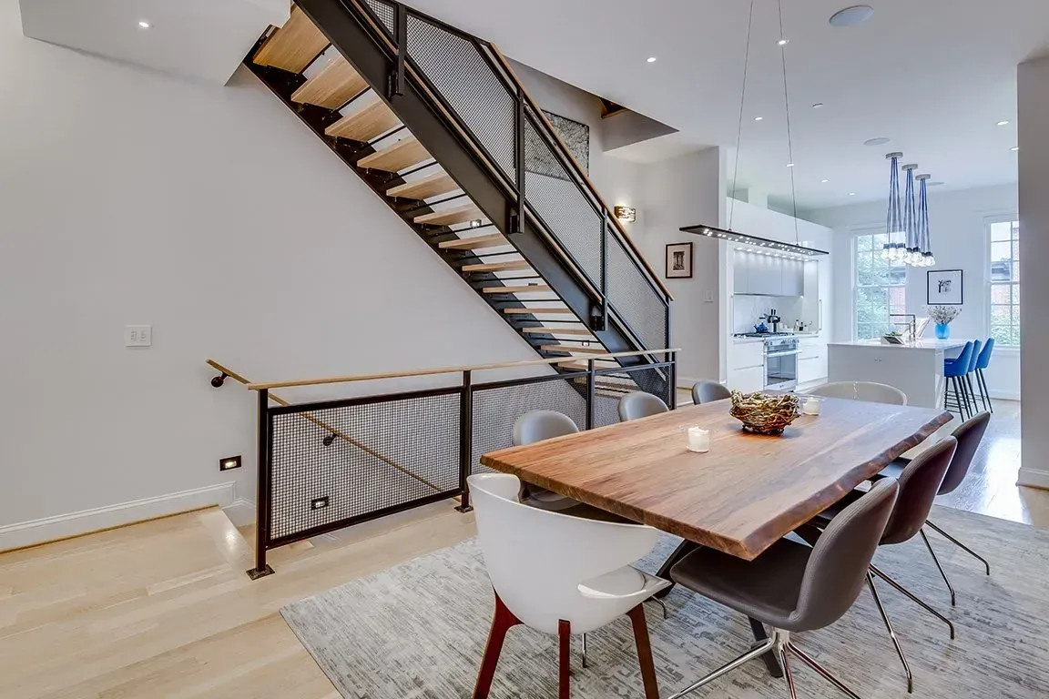 A dining room with a wooden table and chairs and a staircase.