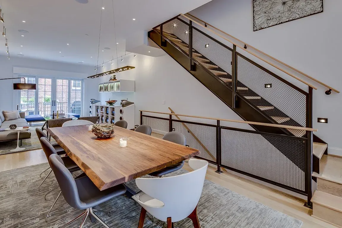 A dining room with a wooden table and chairs and stairs leading up to the second floor.