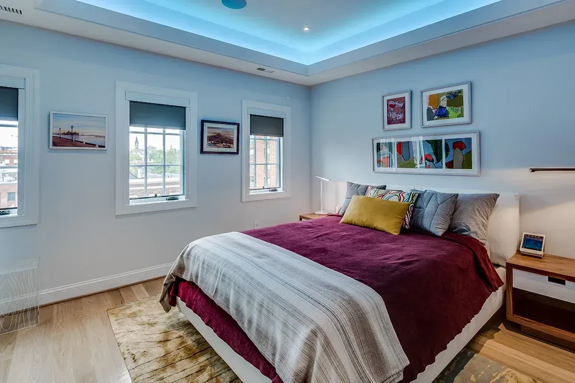 A bedroom with a bed , nightstand , and paintings on the wall.