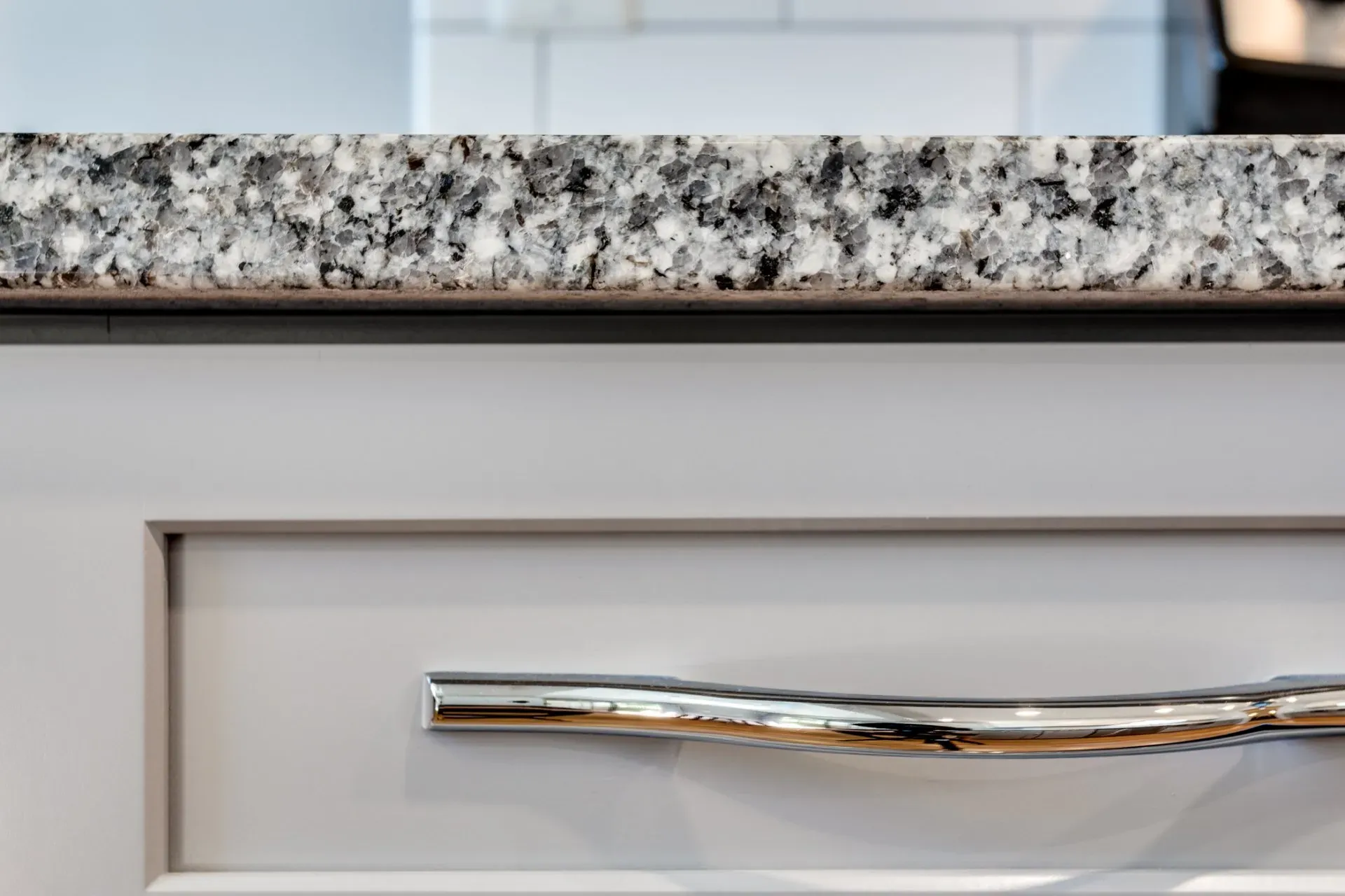 A close up of a drawer with a chrome handle and a granite counter top.