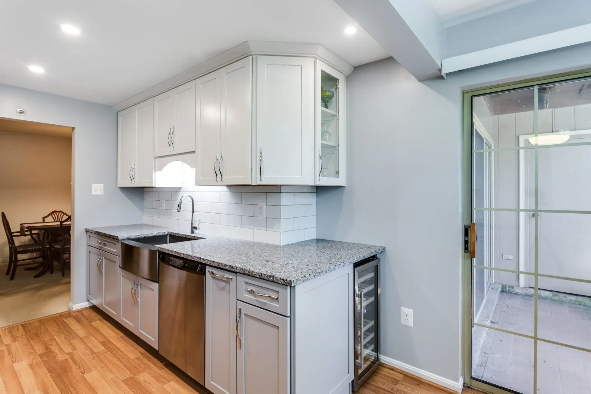 A kitchen with white cabinets , granite counter tops , stainless steel appliances and a sliding glass door.