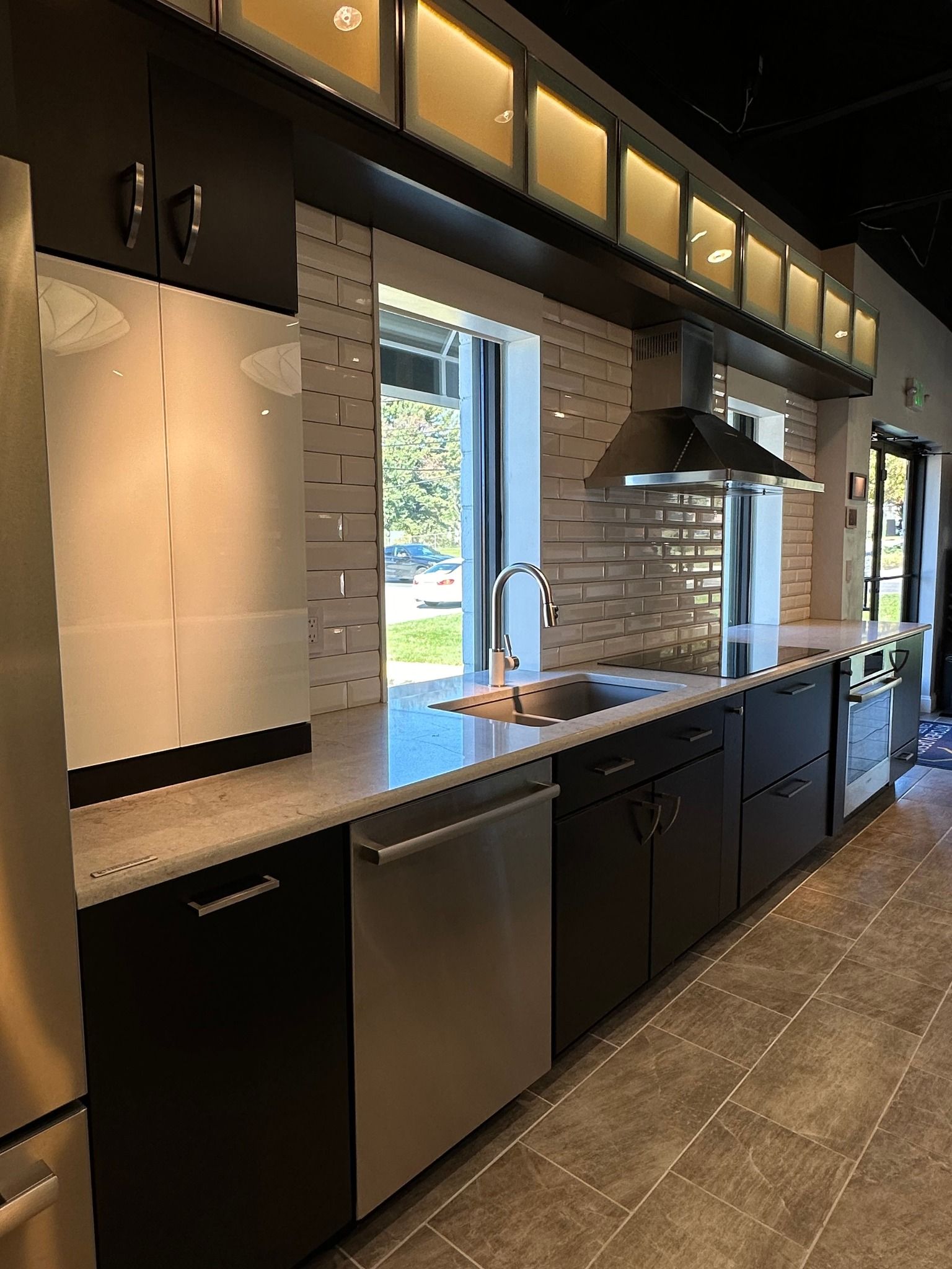 A kitchen with black cabinets , stainless steel appliances , a sink and a window.
