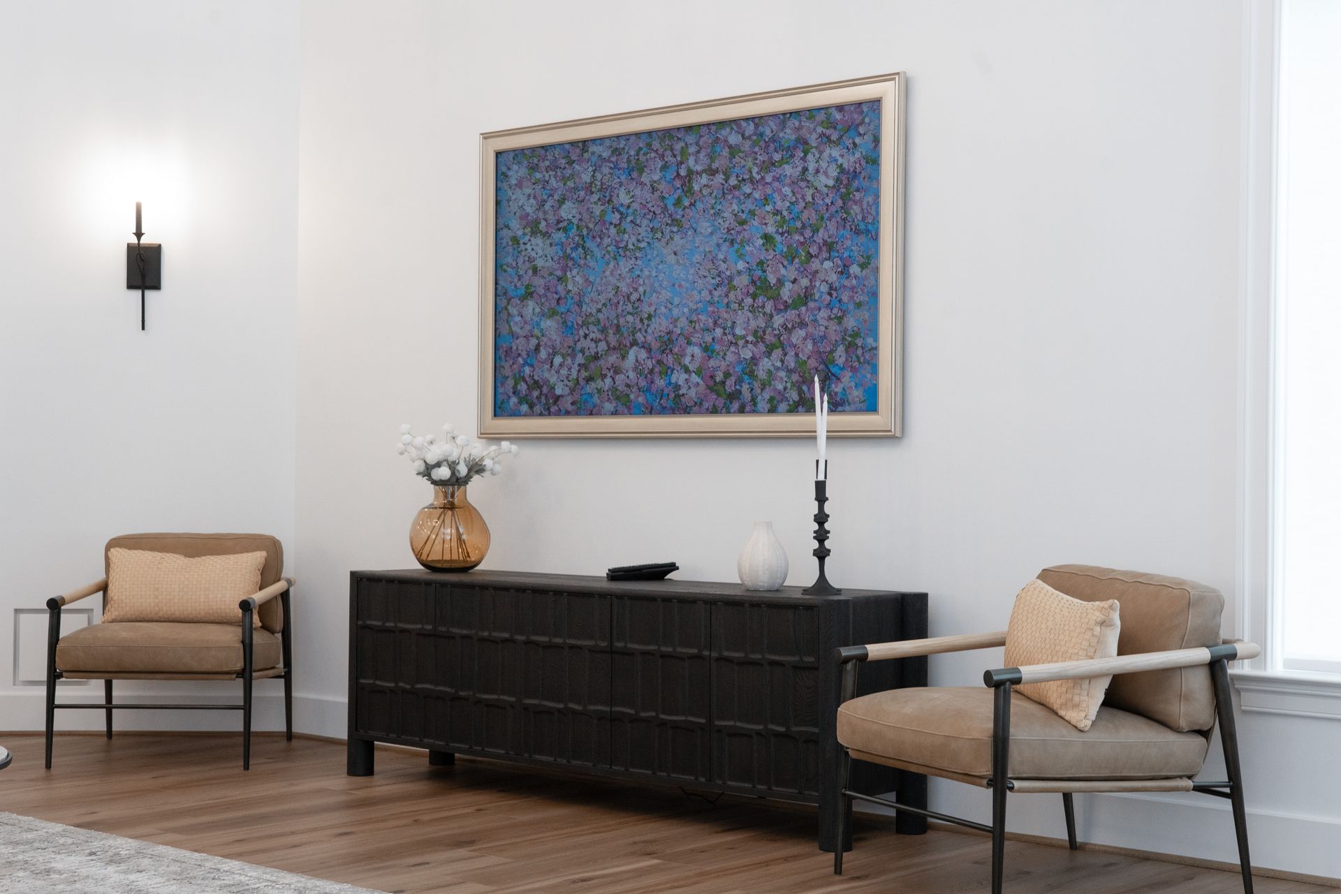 A living room with two chairs , a dresser , and a painting on the wall.