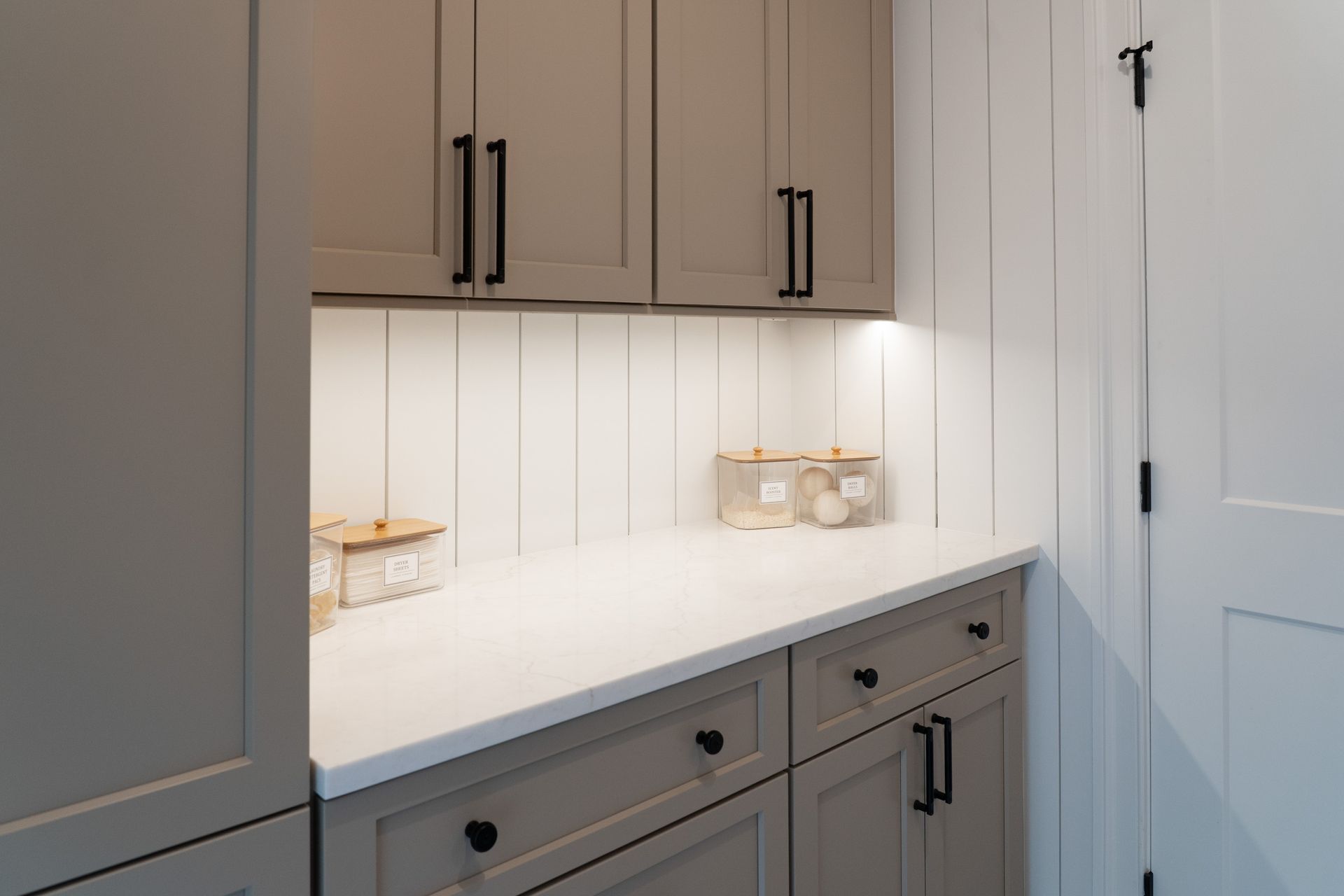 A laundry room with gray cabinets and white counter tops.