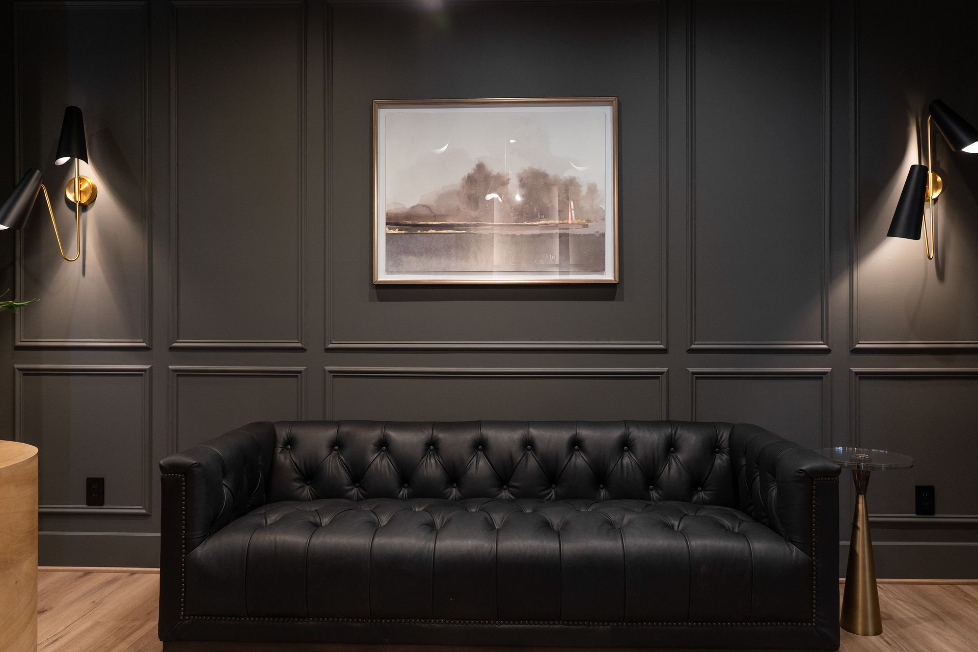 A black leather couch is sitting in a living room with a picture on the wall.