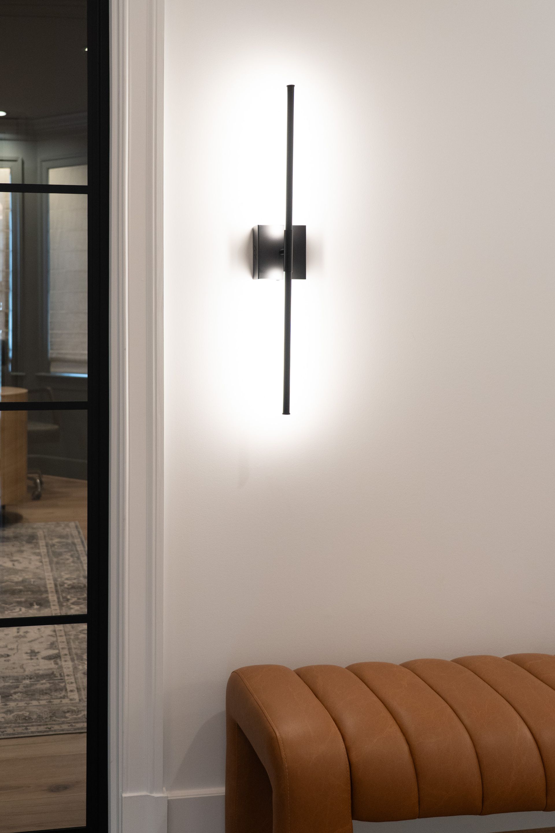 A brown bench is sitting next to a wall with a light on it.