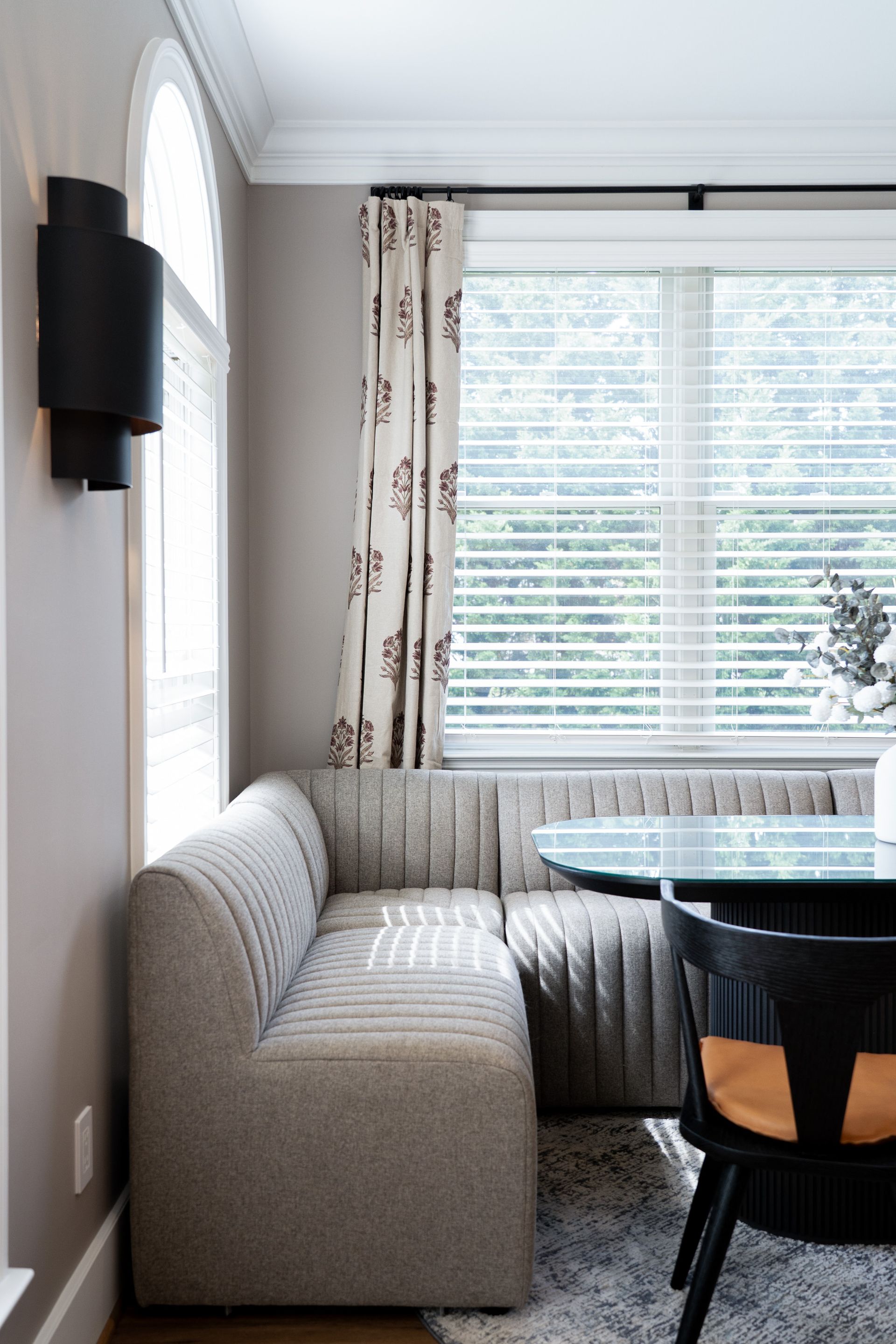 A dining room with a couch , table and chairs in front of a window.