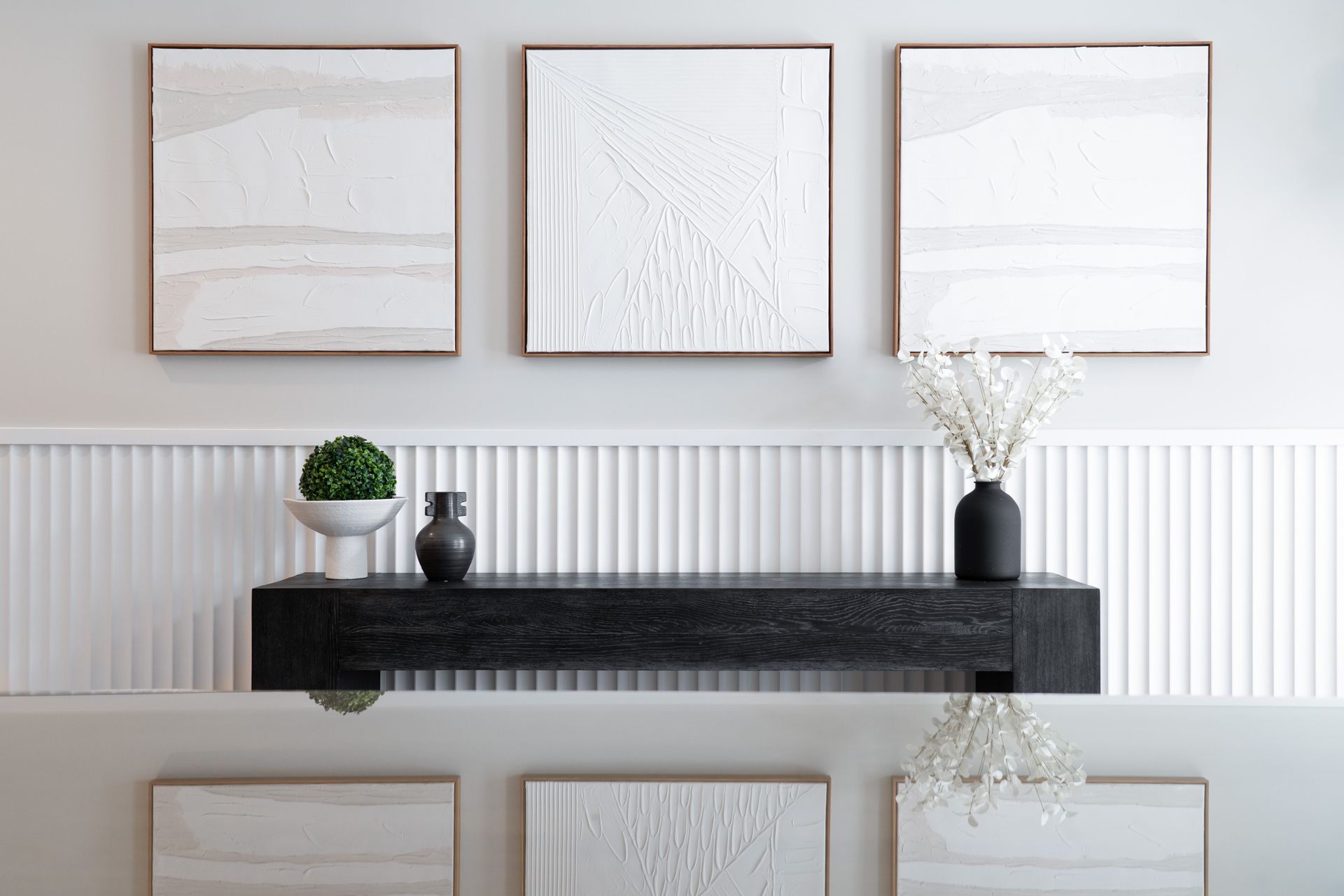 There are three paintings on the wall above a shelf.