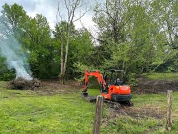 A red excavator is driving through a grassy field.
