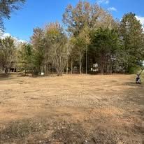 A large empty field with trees in the background and a lawn mower in the foreground.
