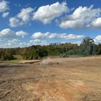 A dirt field with trees in the background and a blue sky with clouds.