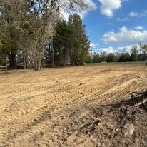 A large dirt field with trees in the background on a sunny day.