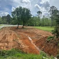 A dirt field with trees and a road in the background.