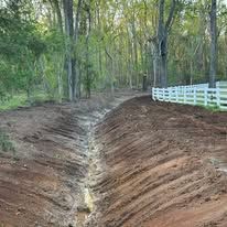 A dirt road in the middle of a forest next to a white fence.