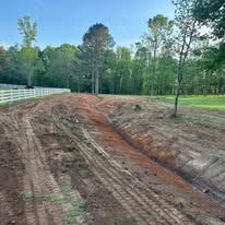 A dirt road going through a field with a white fence in the background.