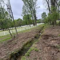 A stream running through a lush green forest next to a white fence.