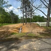 A dirt road with a white fence and trees in the background.
