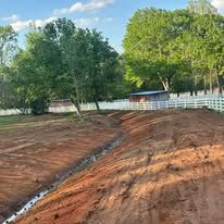 A dirt road with a white fence and trees in the background.