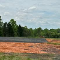 A large dirt field with trees in the background and a road in the foreground.