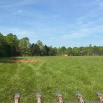 A large grassy field with a wooden fence in the foreground and trees in the background.