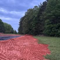 A road with red dirt on the side of it and trees in the background.