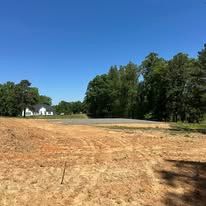 A large dirt field with trees in the background and a house in the background.