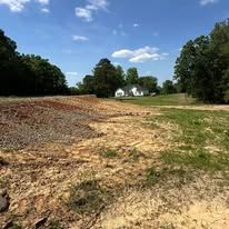 A dirt road going through a field with a house in the background.