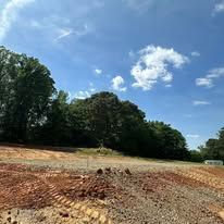 A dirt road with trees in the background and a blue sky with clouds.