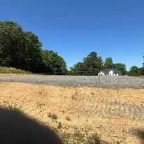 A gravel road going through a field with trees in the background.