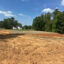 A dirt field with trees in the background and a house in the background.