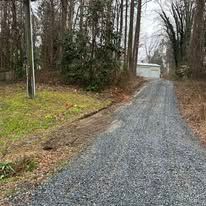 A gravel road leading to a house in the woods.