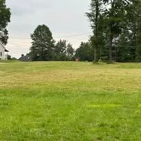 A large grassy field with trees in the background and a house in the background.