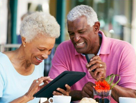an elderly couple is sitting at a table looking at a tablet .