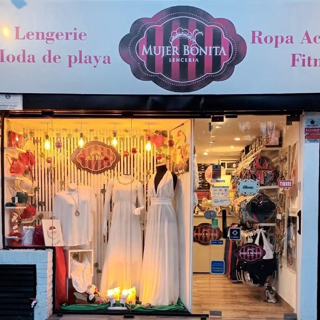 Fachada de una tienda de ropa de playa con vestidos blancos expuestos y un letrero rosa que dice