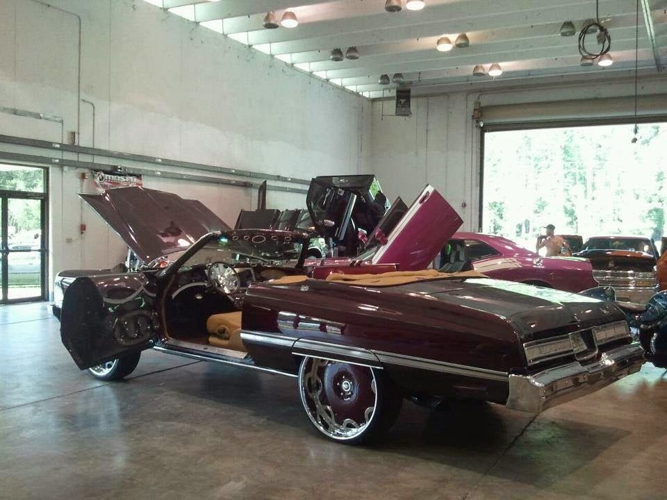 A purple car with the hood up is parked in a garage