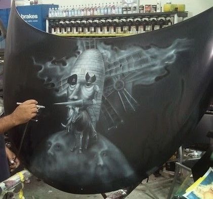 A man is painting a picture on the hood of a car