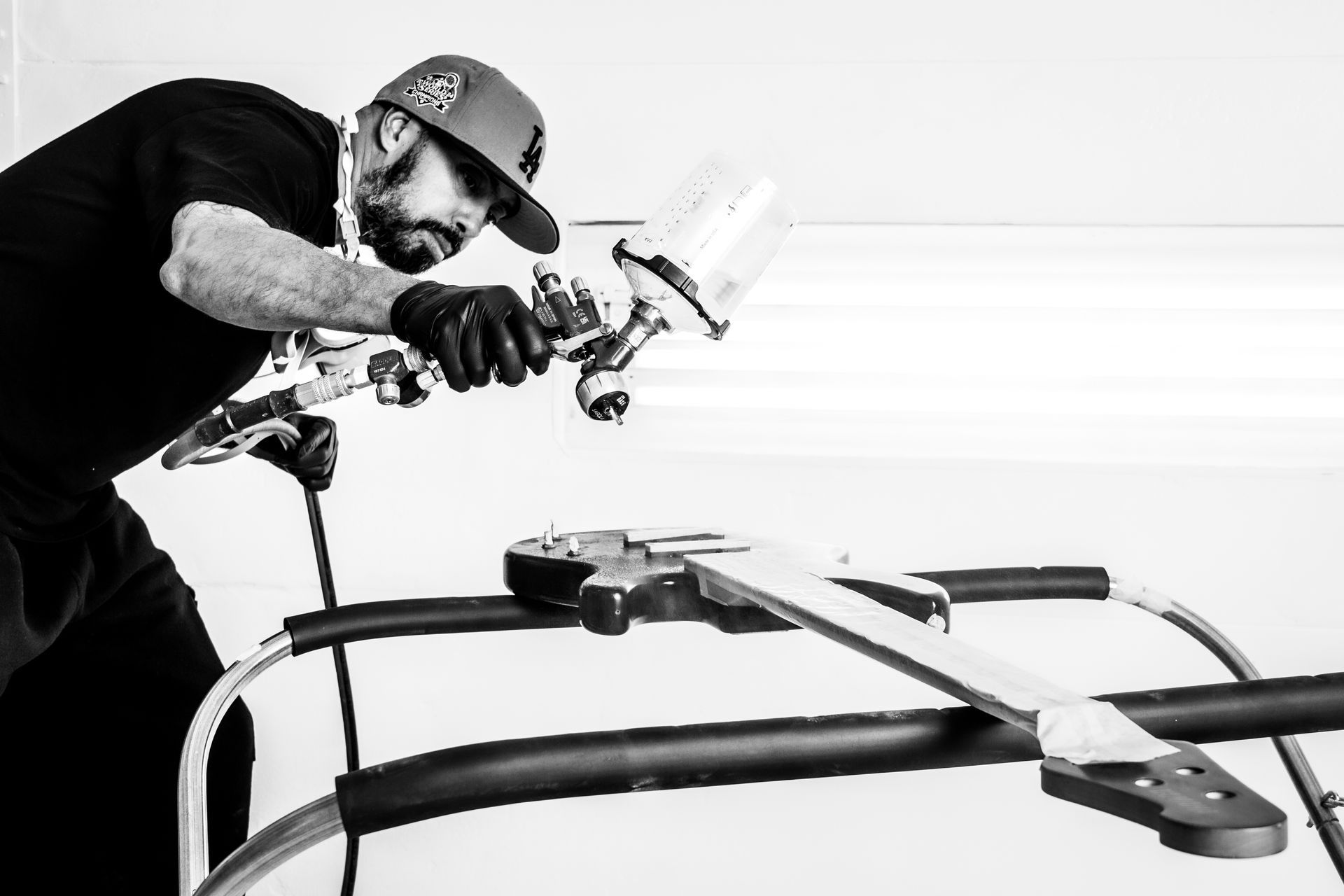 A black and white photo of a man spray painting a piece of metal.