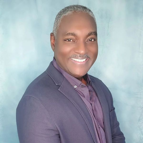 A man wearing a purple jacket and a purple shirt is smiling for the camera.